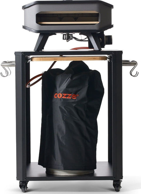 Ein schwarzer Outdoor-Pizzaofen steht auf einem Metallwagen mit zwei seitlichen Haken, einem Holzgriff und Rädern. Darunter befindet sich eine 10-kg-Gasflasche, die durch den Cozze Überzug für Gasflasche 10 kg von Cozze vor Witterungseinflüssen geschützt ist.