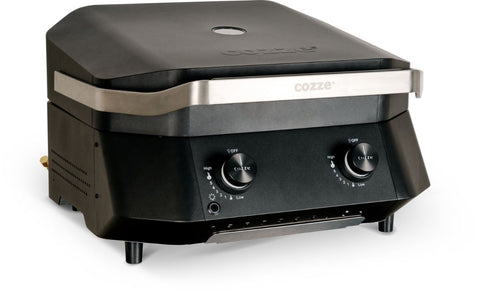Der Cozze G-500 Plancha mit Deckel, Gas 50mbar - CH-Regler ist ein schwarzer Tisch-Gasgrill aus Edelstahl in modernem Design mit zwei Bedienknöpfen und dem Markennamen "Cozze" auf der Vorderseite.