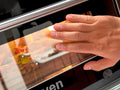 Eine Hand reinigt die Glastür eines Resto Italia Hooven 341 - Elektro Pizzaofen (Digital) mit einem Tuch oder Schwamm. Im Inneren wird Essen – möglicherweise eine leckere neapolitanische Pizza – zubereitet.
