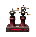 Zwei manuelle Kaffeemühlen im Vintage-Stil mit Holzgriffen und verzierten Sockeln auf einem Räucherwerk-Ständer weisen ein rot-schwarzes Wirbeldesign auf, das an das elegante Metallic-Finish des Bundle Pfeffermühle & Salzmühle mit Sockel – RED DEVIL von Jungo Design erinnert.