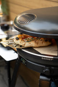 In einem Gozney Arc Gas Pizzaofen Off Black wird eine Pizza gebacken, die Temperatur auf dem Display zeigt 432 °C an. Die Pizza ruht auf einem Stein, wird von einer Schaufel gestützt und ist teilweise aus dem Ofen in einem einladenden Außenküchenbereich.