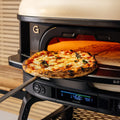 Eine frisch gebackene Pizza auf einer Schaufel wird aus dem Gozney Neapolitanischer Bogen für Dome (Gen 2) von Gozney entnommen, wobei die Digitalanzeige des modernen Ofens 468°F anzeigt.