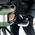 Eine Person in schwarzer Jacke und Handschuhen bedient fachmännisch einen Gozney Ofensims & Frontablage für Tread-Pizzaofen für den Außenbereich, dessen leuchtendes Grün und Schwarz einen Kontrast zum schneebedeckten Boden bildet, während sie ein silbernes halbrundes Tablett in den auf einem Stativ stehenden Ofen schiebt.