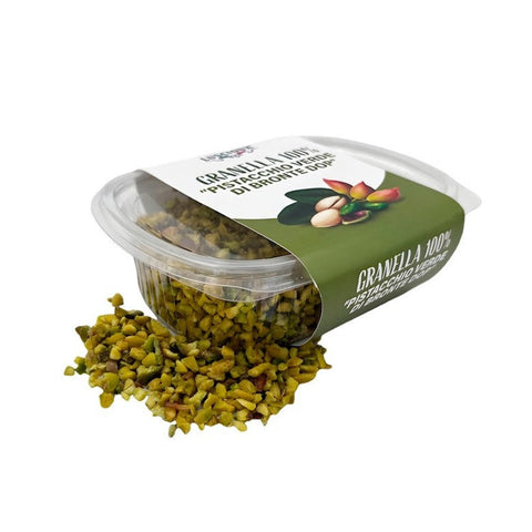 Ein durchsichtiger Plastikbehälter mit der Aufschrift "Luscioux Gehackte Pistazien Bronte DOP 100 g" liegt auf der Seite, und die gehackten Pistazien fallen auf eine weiße Fläche.
