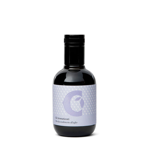 Eine dunkle Glasflasche mit schwarzem Verschluss und hellviolettem Etikett mit abstraktem Design, darunter ein stilisierter Halbmond und eine Knoblauchzehe, trägt den Text: „Gli Aromatizzati Olio condimento all'aglio“. Diese 100-ml-Flasche „Olivenöl extra vergine mit Knoblauch-Aroma“ von Ciccolella bietet extra natives Olivenöl mit Knoblaucharoma.