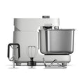 Wir präsentieren die Ooni Halo Pro Spiral-Knetmaschine von Ooni, eine elegante Küchenmaschine mit Spiral-Knettechnologie. Sie verfügt über eine Edelstahlschüssel, ein hellgraues Gehäuse und enthält einen Rührer, Schneebesen und Knethaken – ideal, um jedes Mal einen perfekten Pizzateig zuzubereiten.
