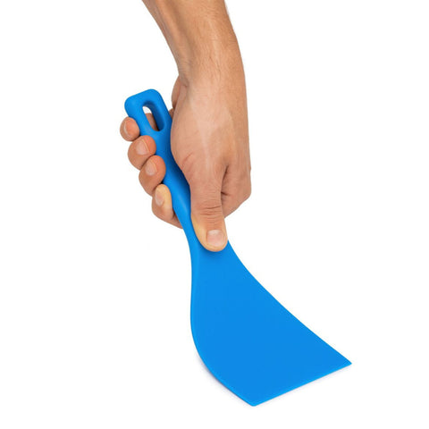 Eine Hand hält den Gi.Metal Profi Teigspachtel Flexibel, einen blauen, haltbaren Polymerspachtel mit breiter, flacher Klinge und Griffloch - perfekt zum Formen von Teigkugeln - vor einem weißen Hintergrund.