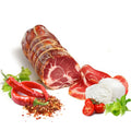 Eine ganze Rolle Capocollo Calabrese Scharf (Coppa) - am Stück 700G von Madeo ist mit einer Schnur zusammengebunden und teilweise in Scheiben geschnitten, wodurch die marmorierte Textur sichtbar wird. Zu dieser feinen mediterranen Vorspeise gibt es ein Stück Mozzarellakäse, halbierte Kirschtomaten, Blattgemüse, rote Chilischoten und zerstoßene rote Pfefferflocken auf weißem Hintergrund.