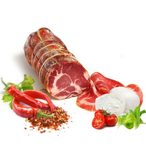 Eine ganze Rolle Capocollo Calabrese Scharf (Coppa) - am Stück 700G von Madeo ist mit einer Schnur zusammengebunden und teilweise in Scheiben geschnitten, wodurch die marmorierte Textur sichtbar wird. Zu dieser feinen mediterranen Vorspeise gibt es ein Stück Mozzarellakäse, halbierte Kirschtomaten, Blattgemüse, rote Chilischoten und zerstoßene rote Pfefferflocken auf weißem Hintergrund.