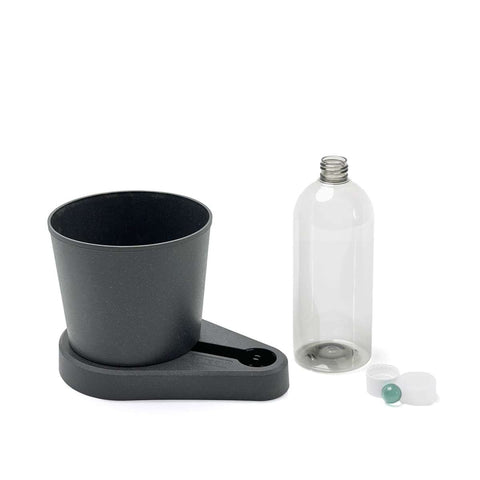 Ein schwarzer, selbstbewässernder Kräuterheld von Greevi steht neben einer leeren, durchsichtigen Flasche mit weißem Deckel und einer kleinen blauen Kugel, die daneben liegt.