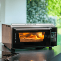 Der Effeuno Pizzaofen P134H 509°C Evolution mit Biscotto Pizzastein, ausgestattet mit einem digitalen Bedienfeld und PID-Temperaturregelung, backt eine Pizza mit geschmolzenem Käse und Belag. Die Innenbeleuchtung des Ofens beleuchtet die neapolitanische Pizzaqualität, während im Hintergrund durch ein Fenster üppiges Grün sichtbar ist.