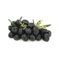 Ein Haufen von Nadias Olive Nere al Forno – schwarze Oliven gebacken 190 g mit glänzender Oberfläche ist mit kleinen grünen Olivenblättern und winzigen gelbgrünen Blüten garniert und ähnelt einem köstlichen Antipasti-Aufstrich. Die Oliven und Garnierungen sind vor einem schlichten weißen Hintergrund angeordnet.