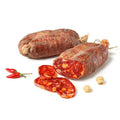 Zwei Stücke Madeo Soppressata Salami BIO (Scharf) werden auf einem weißen Hintergrund präsentiert. Eine Wurst ist ganz, während die andere aufgeschnitten ist, sodass das reichhaltige, marmorierte Innere sichtbar ist. Zu den Würsten gibt es ein paar kleine rote Chilischoten und zwei Knoblauchzehen.